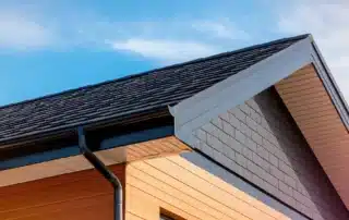 Close-up view of a skilled roofer inspecting the shingles of a residential roof in New Britain, CT, with a well-maintained home exterior in the background.
